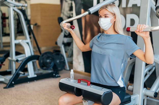 Donna che si esercita in palestra con maschera medica e attrezzature