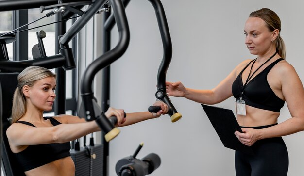 Donna che si esercita in palestra e allenatore che tiene appunti