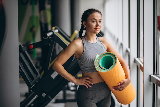 Donna che si esercita in palestra tenendo la stuoia di yoga