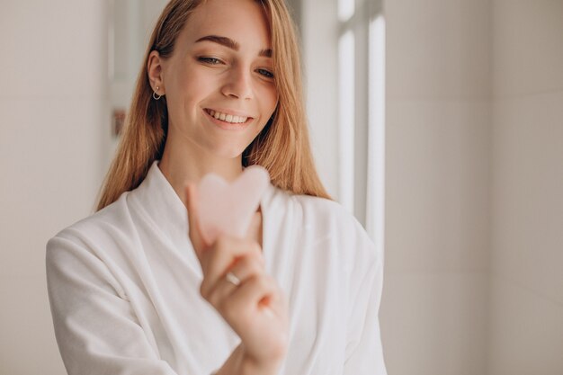 Donna che si fa automassaggio con pietra gua sha al quarzo rosa