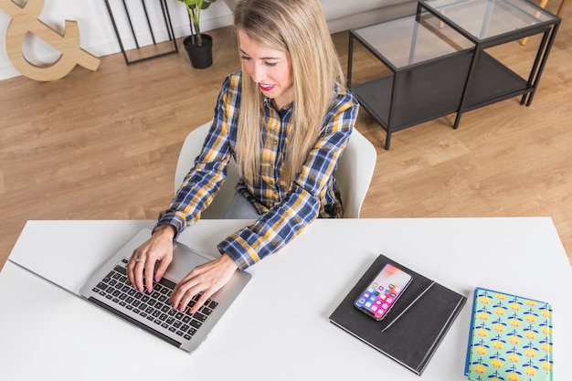 Donna che si siede al tavolo e digitando sulla tastiera del computer portatile