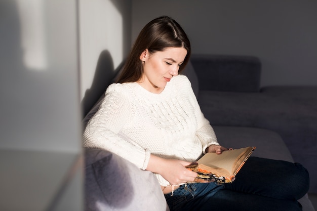 Donna che si siede con il libro sul divano