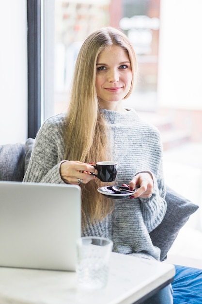 Donna che si siede con tazza e piattino al computer portatile