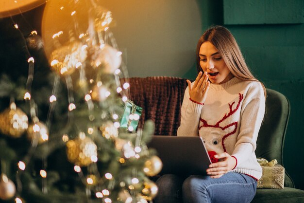 Donna che si siede dall'albero di Natale e dalle vendite online di compera