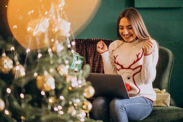 Donna che si siede dall'albero di Natale e dalle vendite online di compera