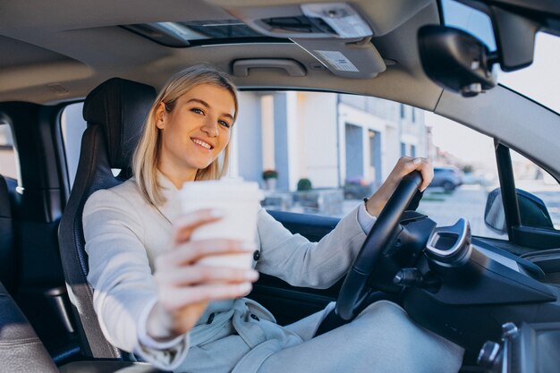 Donna che si siede dentro l'elettro automobile mentre si carica con una tazza di caffè