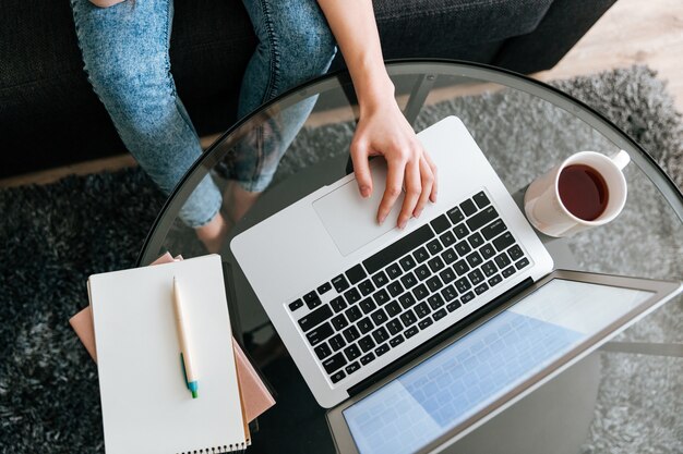 Donna che si siede e che per mezzo del computer portatile sulla tavola di vetro a casa