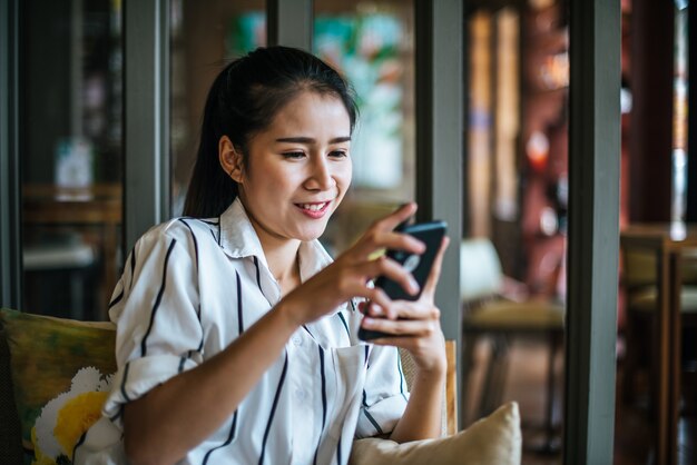 Donna che si siede e giocando il suo smart phone al caffè