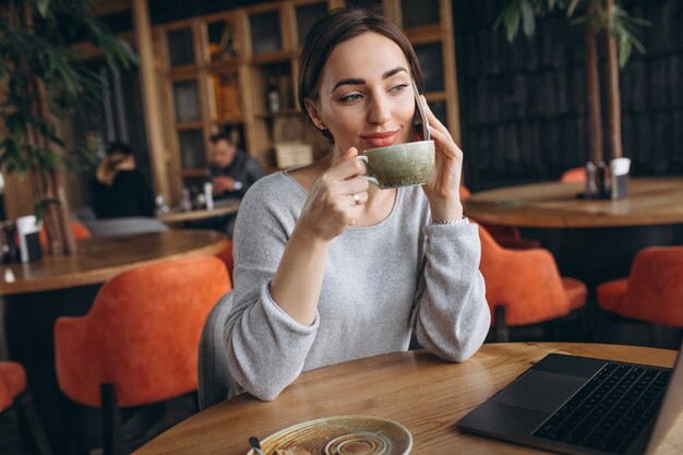 Donna che si siede in un caffè bevendo caffè e lavorando su un computer