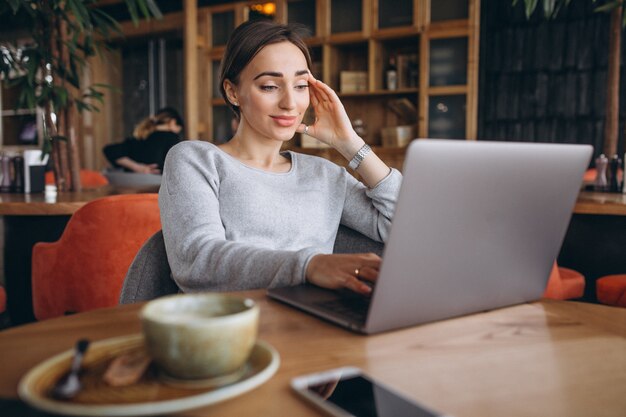 Donna che si siede in un caffè bevendo caffè e lavorando su un computer