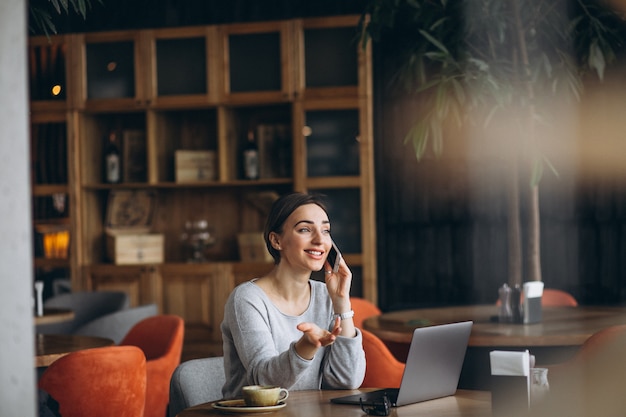 Donna che si siede in un caffè bevendo caffè e lavorando su un computer