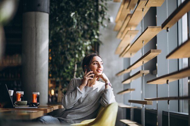 Donna che si siede in un caffè bevendo caffè e lavorando su un computer