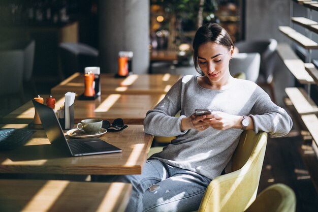 Donna che si siede in un caffè bevendo caffè e lavorando su un computer