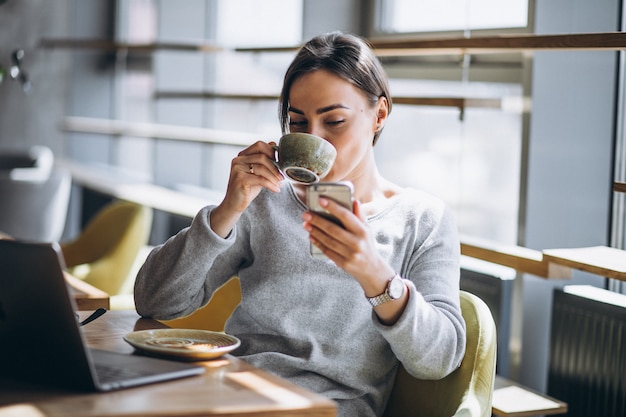 Donna che si siede in un caffè bevendo caffè e lavorando su un computer