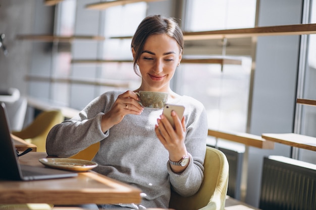 Donna che si siede in un caffè bevendo caffè e lavorando su un computer