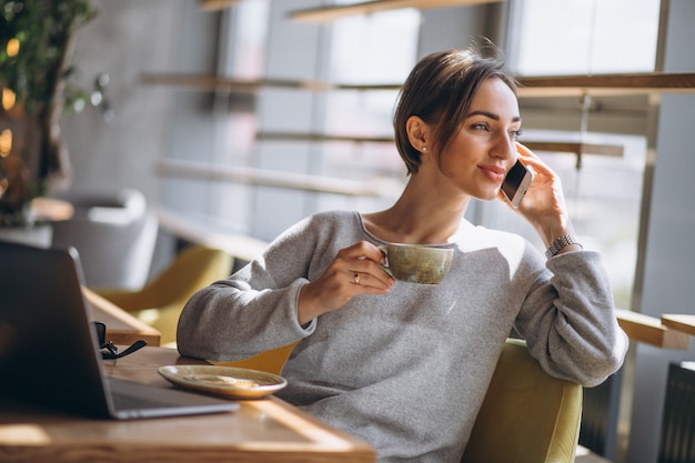 Donna che si siede in un caffè bevendo caffè e lavorando su un computer