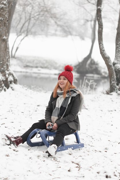 Donna che si siede su una slitta alla luce del giorno di inverno