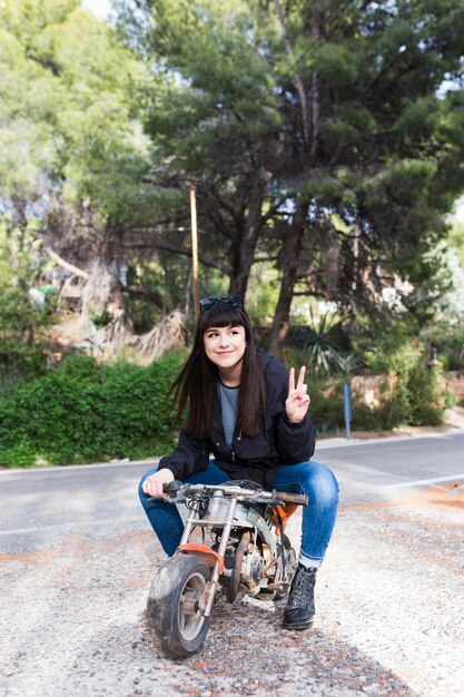 Donna che si siede sul motociclo e che mostra il segno di vittoria