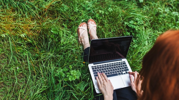 Donna che si siede sull&#39;erba con il computer portatile