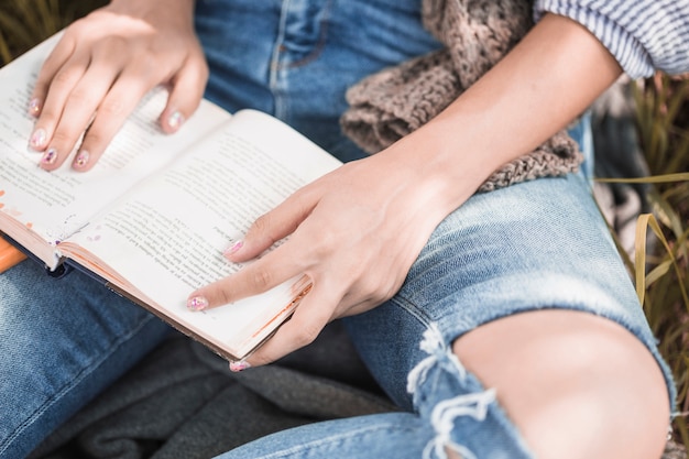 Donna che si siede sull&#39;erba con il libro e seguendo il testo a mano