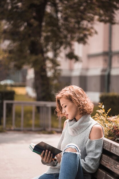 Donna che si siede sulla panchina e libro di lettura nel parco