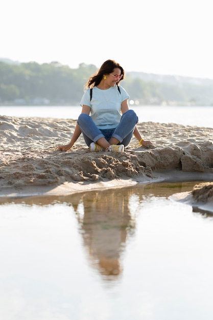 Donna che si siede sulla sabbia alla spiaggia