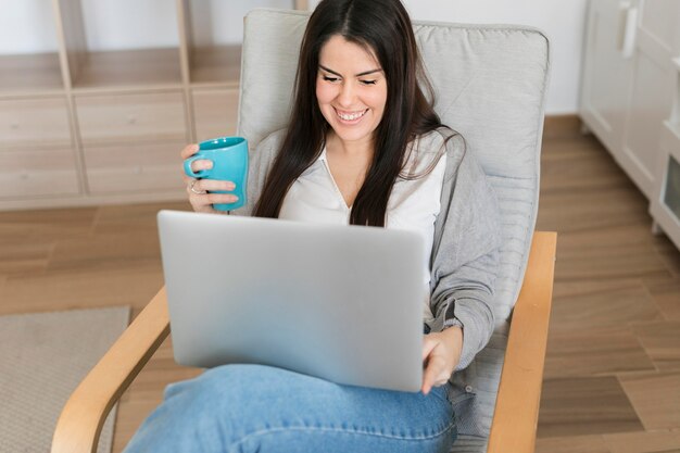 Donna che si siede sulla sedia con il computer portatile e che beve caffè