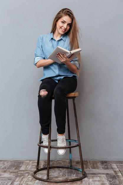 Donna che si siede sulla sedia e sul libro di lettura