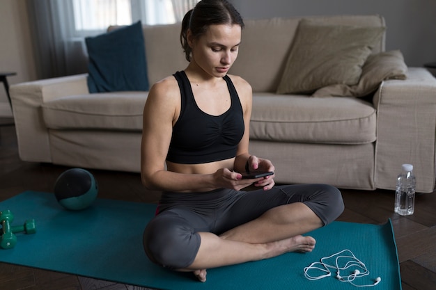 Donna che si siede sulla stuoia di yoga e che esamina telefono