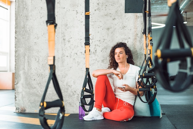 Donna che si siede vicino alla cinghia di forma fisica che ascolta la musica sul telefono cellulare