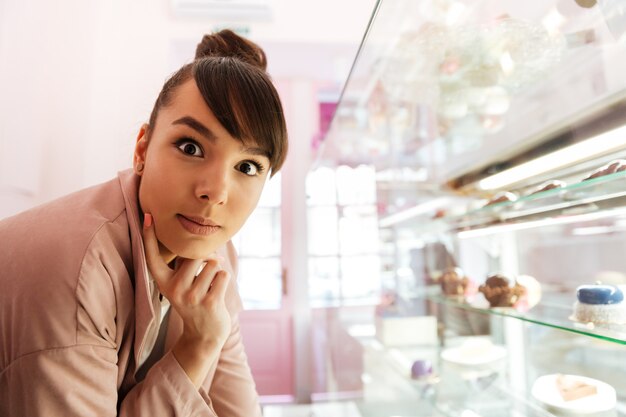 Donna che sta alla vetrina di vetro con patries dentro il caffè