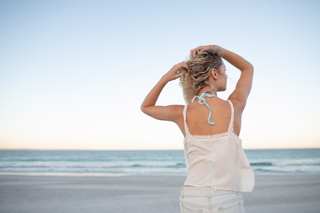 Donna che sta con le mani in suoi capelli sulla spiaggia