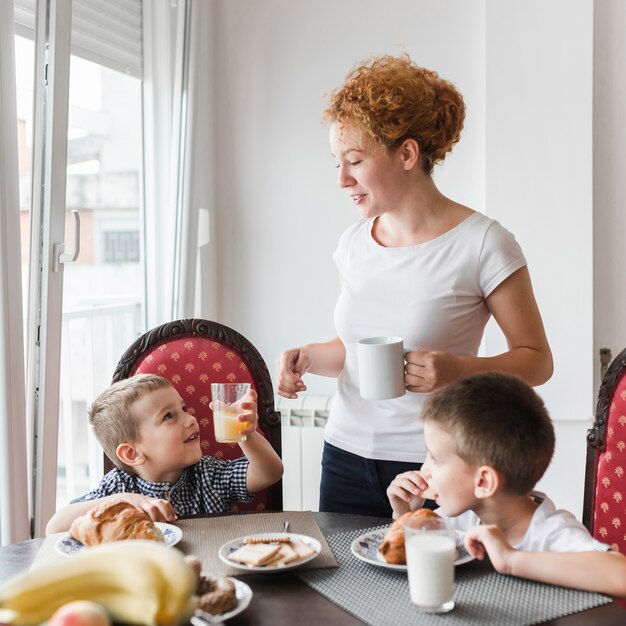 Donna che sta vicino ai suoi bambini che mangiano prima colazione sana