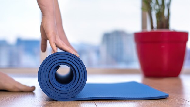 Donna che svolge un tappetino yoga blu per la formazione a casa