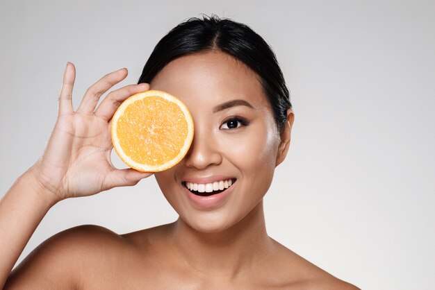 donna che tiene fette d'arancia vicino al suo viso