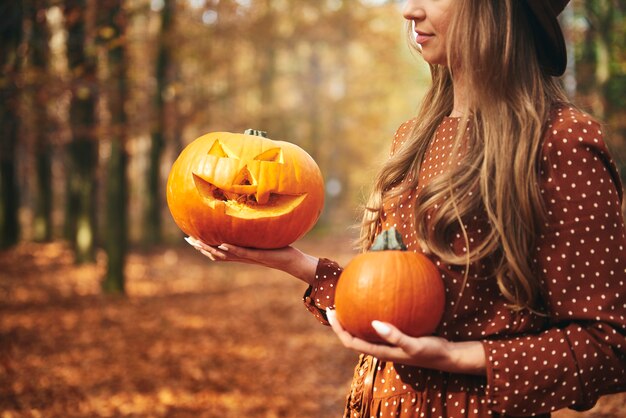 Donna che tiene la zucca di halloween nella foresta autunnale