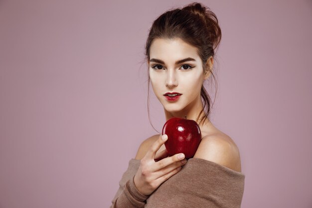 donna che tiene mela rossa sul rosa