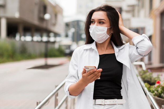 Donna che tiene smartphone e indossa una maschera mentre va al lavoro