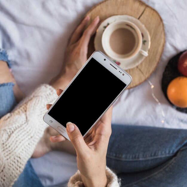 Donna che tiene smartphone e tazza di caffè