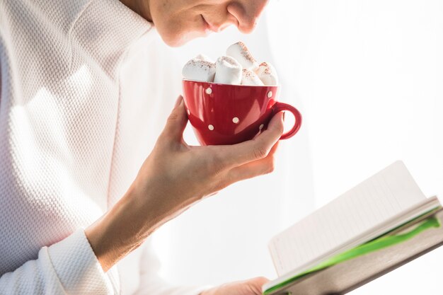 Donna che tiene tazza con marshmallow e libro