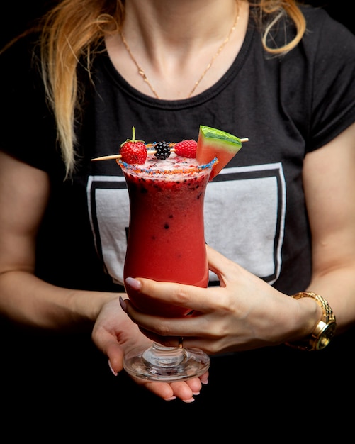Donna che tiene un bicchiere di cocktail di frutta guarnito con lampone mora fragola e anguria