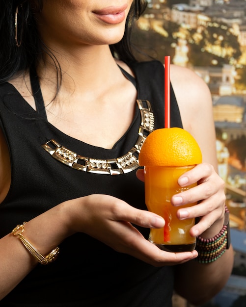 Donna che tiene un bicchiere di succo d'arancia guarnito con l'arancia divisa in due