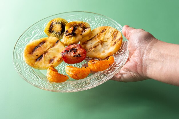 Donna che tiene un piatto di frutta alla griglia su sfondo verde