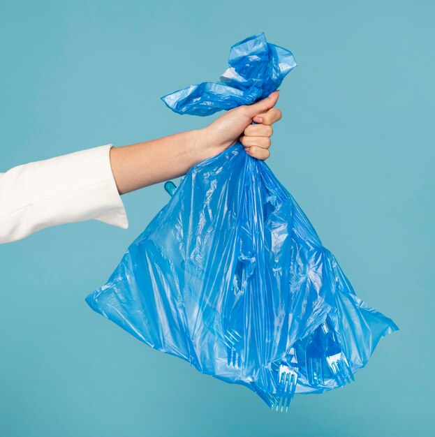 Donna che tiene un sacchetto della spazzatura di plastica blu