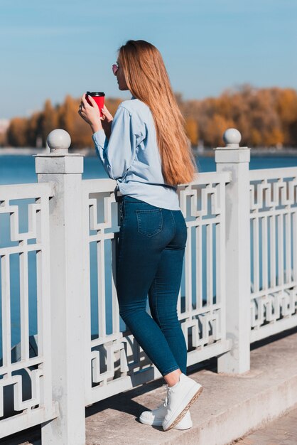 Donna che tiene una tazza di caffè e che riposa sull'inferriata