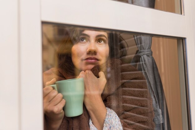 Donna che tiene una tazza di caffè mentre è coperto con una coperta