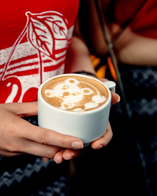 Donna che tiene una tazza di cappuccino con latte art a forma di orso