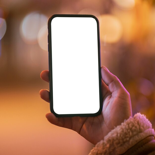 Donna che tiene uno smartphone in bianco con effetto bokeh intorno