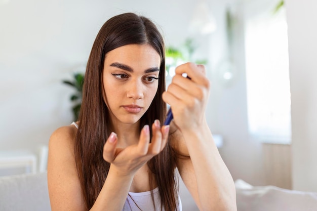 Donna che usa la lancetta sul dito Donna che esegue il test della glicemia a casa in un soggiorno Controllo del diabete