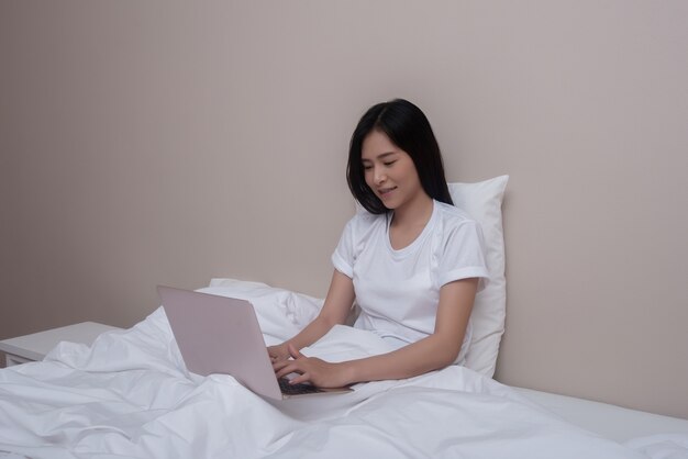 Donna che usando seduta sorridente del computer portatile sul letto